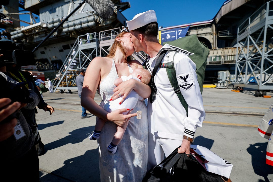 Saylor Caleb Atkins kisses his wife McKenzie Adkins, as she holds their baby after the US Navy Nimitz-class aircraft carrier USS Abraham Lincoln returned home following an extended deployment in the Middle East at Naval Base Coronado in San Diego, California, on Oct. 8, 2026.
